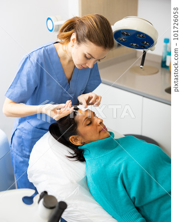 Woman patient receiving forehead injection at clinic Woman patient receiving forehead injection at clinic 101726058
