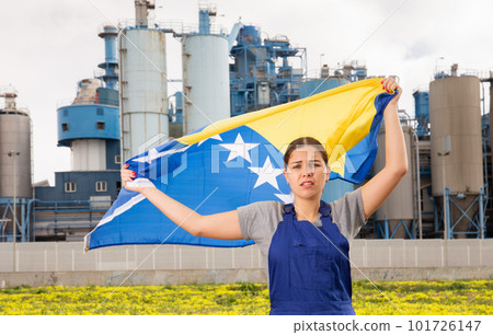 in countryside,frustrated worker in overalls stands in front of factory building with Bosnian flag in countryside,frustrated worker in overalls stands in front of factory building with Bosnian flag 101726147