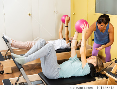 Teens doing pilates with balls under the supervision of female trainer 101726218