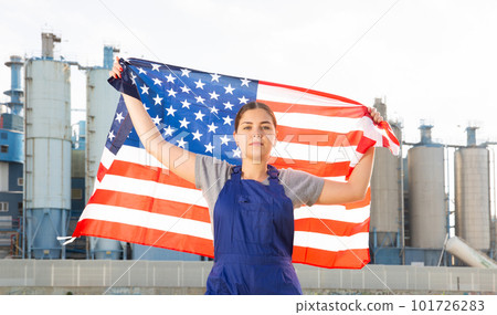 Calm young woman worker with flag of the USA against background of factory 101726283