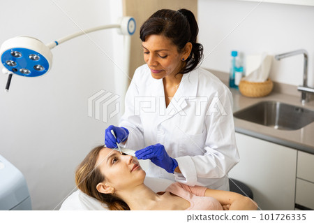 Beautician using white pencil and ruler for marking skin of young woman 101726335