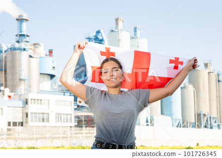 Happy girl with flag of georgia standing in front of industrial scenery 101726345