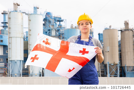 Young female engineer in helmet waving state flag of Georgia while standing in front of big tanks at chemical plant 101726445