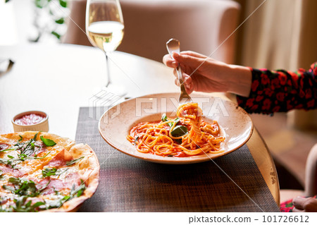 Italian Trattoria. Woman eats Italian pasta with tomato, meat. Spaghetti Bolognese wind it around a fork with a spoon. Parmesan cheese Italian Trattoria. Woman eats Italian pasta with tomato, meat. Spaghetti Bolognese wind it around a fork with a spoon. Parmesan cheese 101726612