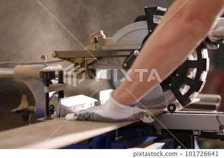 Man in protective gloves works with miter saw cutting board 101726641