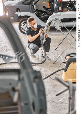 Small Garage. The mechanic works with a grinding tool. Sanding of car elements. Painting car service. Repairing car section after the accident. Small Garage. The mechanic works with a grinding tool. Sanding of car elements. Painting car service. Repairing car section after the accident. 101726646