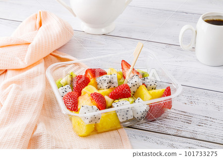 Fruit salad of pineapple, strawberries, kiwi and pitahaya in a plastic container on a wooden background. Fruit salad of pineapple, strawberries, kiwi and pitahaya in a plastic container on a wooden background. 101733275