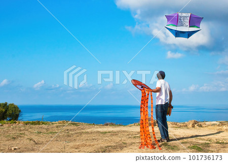 A man flying a kite on the coast with the blue sea in the background 101736173