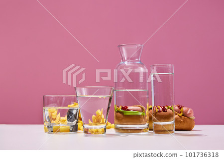 Hot dog sandwich with sauses near glasses with water on white table over pink background. French fries menu 101736318