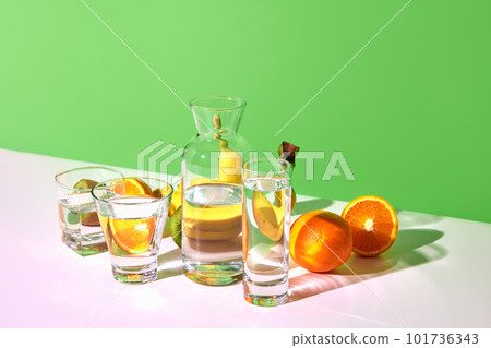 Still life with fresh fruits kiwi, banana, orange and glasses with water on table over green background. Bright colors. Fruit detox 101736343