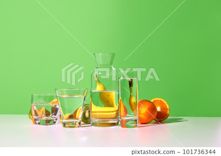 Still life with fresh fruits kiwi, banana, orange and glasses with water on table over green studio background. Bright colors. Food reflection Still life with fresh fruits kiwi, banana, orange and glasses with water on table over green studio background. Bright colors. Food reflection 101736344