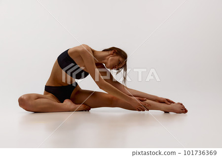 Beautiful young girl with tanned, fit, slim body posing in black underwear, stretching against white studio background Beautiful young girl with tanned, fit, slim body posing in black underwear, stretching against white studio background 101736369