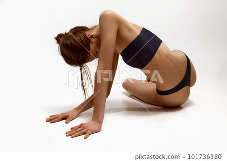 Young girl with fit, slim, healthy body in black underwear posing on floor against white studio background 101736380