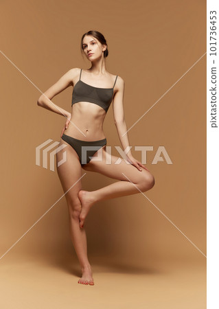 Full-length portrait of young beautiful girl with slim, fit body shape, posing in underwear against light brown studio background 101736453