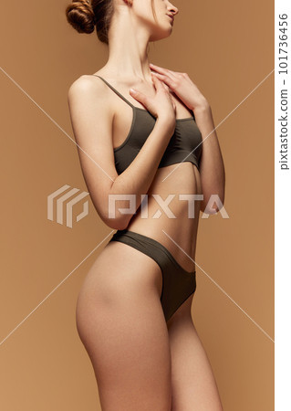 Fit and healthy. Cropped Image of slim female body in cotton underwear posing against light brown studio background Fit and healthy. Cropped Image of slim female body in cotton underwear posing against light brown studio background 101736456