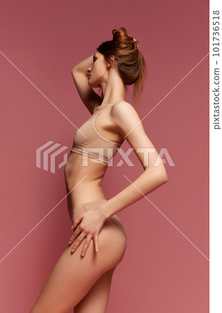 Side view portrait of young slim girl posing in beige underwear against pink studio background. Fit, healthy, beautiful body Side view portrait of young slim girl posing in beige underwear against pink studio background. Fit, healthy, beautiful body 101736518