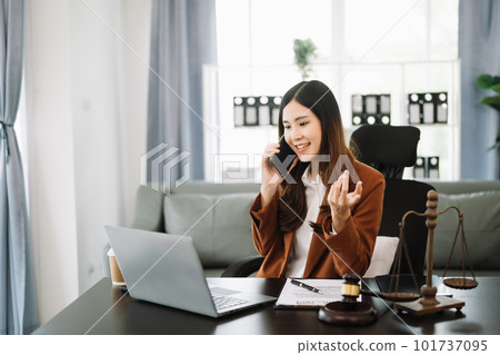 Asian female lawyer chatting online with client on laptop, smartphone  discussing details of lawsuit. in modern office 101737095