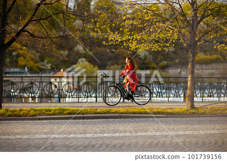 woman in red rain coat outdoors on city street riding bicycle 101739156