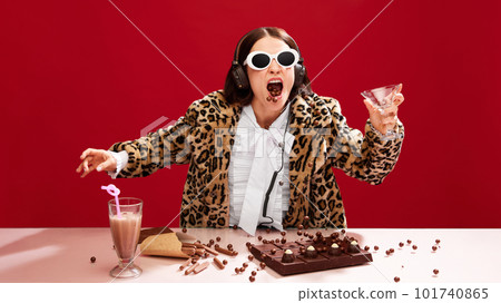 Emotional, eccentric woman in sunglasses and animal print coat, dj on party, playing music and eating chocolate against red background Emotional, eccentric woman in sunglasses and animal print coat, dj on party, playing music and eating chocolate against red background 101740865