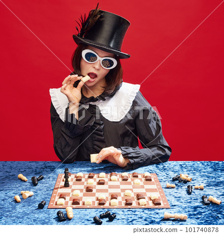Game on. Stylish woman in cylinder hat and sunglasses playing chess with chocolate figures, eating candies against red background Game on. Stylish woman in cylinder hat and sunglasses playing chess with chocolate figures, eating candies against red background 101740878