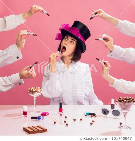 Stylish young woman in black cylinder hat and white blouse applying chocolate colour lipstick over pink background. Multi hands around Stylish young woman in black cylinder hat and white blouse applying chocolate colour lipstick over pink background. Multi hands around 101740947