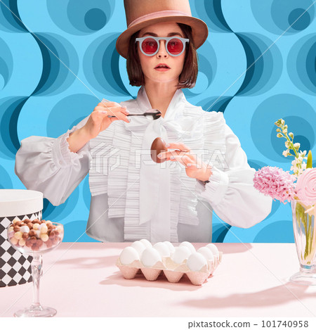 Chocolates lover. Stylish woman in cylinder har and sunglasss eating chocolate eater egg. Blue pattern background 101740958