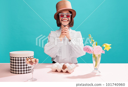 Funny meme emotions. Woman in cylinder hat, holding magnifying glass near mouth and smiling over blue background. Easter chocolate egg 101740960