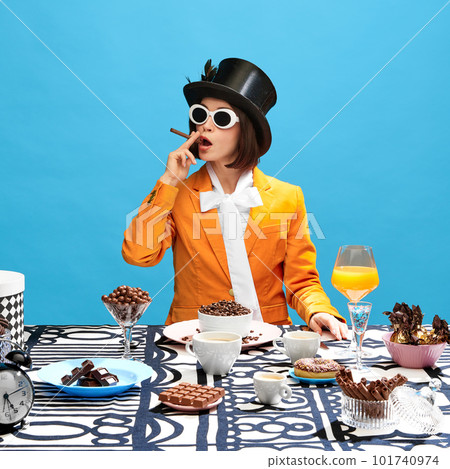 Wonderful woman in cylinder and sunglasses smoking with sweets, sitting at table full of various chocolates over blue background. Sweet tooth Wonderful woman in cylinder and sunglasses smoking with sweets, sitting at table full of various chocolates over blue background. Sweet tooth 101740974