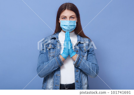 Horizontal photo of calm attractive young female putting hands together, having peaceful facial expression, wearing protective mask and gloves, stay isolated, being in quarantine. Coronavirus concept. Horizontal photo of calm attractive young female putting hands together, having peaceful facial expression, wearing protective mask and gloves, stay isolated, being in quarantine. Coronavirus concept. 101741691