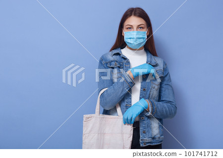 Horizontal picture of good looking attractive young female holding ecobag for shopping, wearing antibacterial mask and gloves, staying safe, going to supermarket for products. Covid19 concept. 101741712