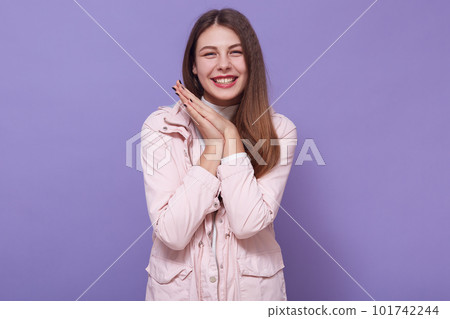 Portrait of peaceful joyful sweet young lady smiling sincerely, having cute smile, keeping hands together, being in good mood, having long hair, wearing casual clothes. People and emotions concept. Portrait of peaceful joyful sweet young lady smiling sincerely, having cute smile, keeping hands together, being in good mood, having long hair, wearing casual clothes. People and emotions concept. 101742244