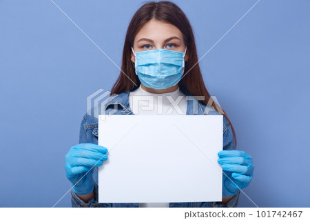 Panic woman with blankpaper for some inscription standing isolated over blue background, young female wearing demin jacket, flu disponsable medical mask and protective gloves. Coronavis, covid concept 101742467