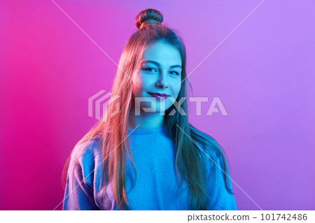 Closeup portrait of young teenager female wearing casual sweater, posing with hair bun, looking smiling directly at camera, posing isolated over pink neon background. People lifestyle concept. 101742486
