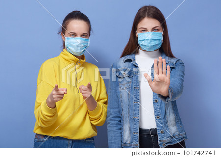 Image of two attractive females being against approaching to them, wearing masks, protecting themselves from potential danger, self isolation, no contacts. People and coronavirus threat concept. 101742741