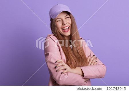 Closeup portrait of laughing woman posing isolated over lilac studio background with folded hands, female wearing rose leather jacket and hat, girl expressing happiness, looking at camera with smile. Closeup portrait of laughing woman posing isolated over lilac studio background with folded hands, female wearing rose leather jacket and hat, girl expressing happiness, looking at camera with smile. 101742945