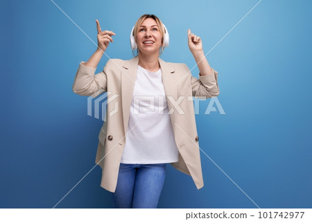 a slender young woman dressed in a white T-shirt and jacket listens to music on headphones 101742977