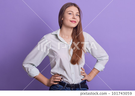 Horizontal indoor shot of attractive beautiful young female covering her mouth with both fists, standing isolated over lilac background in studio, having cunning facial expression. Youth concept. Horizontal indoor shot of attractive beautiful young female covering her mouth with both fists, standing isolated over lilac background in studio, having cunning facial expression. Youth concept. 101743059