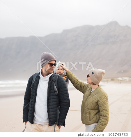 Young father carrying his infant baby boy son in backpack on windy sandy Famara beach, Lanzarote island, Spain. Family travel and winter vacation concept 101745783