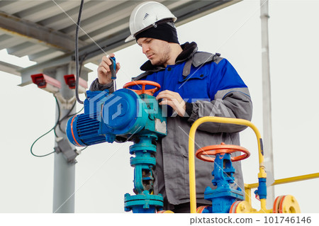 An engineer with a screwdriver repairs equipment at a gas station. Male engineer in helmet and An engineer with a screwdriver repairs equipment at a gas station. Male engineer in helmet and 101746146