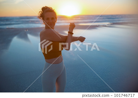happy healthy woman jogger at beach in evening stretching 101746717