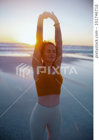 relaxed active sports woman at beach at sunset stretching 101746718