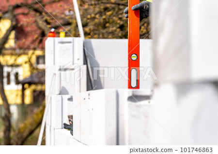 leveling bricks with the help of a spirit level during the construction of the wall of the house 101746863