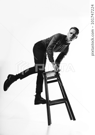 A stylish black and white portrait of a man in a shirt posing on a white cyclorama with a chair, evoking a sense of sophistication and refinement. A stylish black and white portrait of a man in a shirt posing on a white cyclorama with a chair, evoking a sense of sophistication and refinement. 101747224