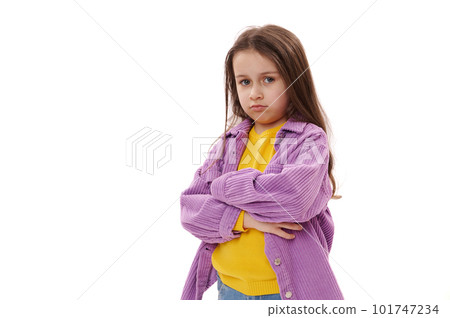Isolated portrait on a white background of a naughty mischievous little girl 5-6 years old, pouting lips in resentment, standing with her arms crossed and looking at the camera with a displeased look 101747234
