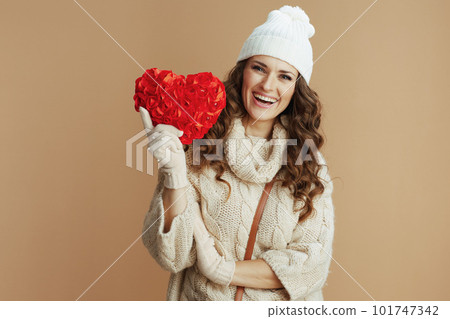 happy woman in beige sweater, mittens and hat against beige 101747342