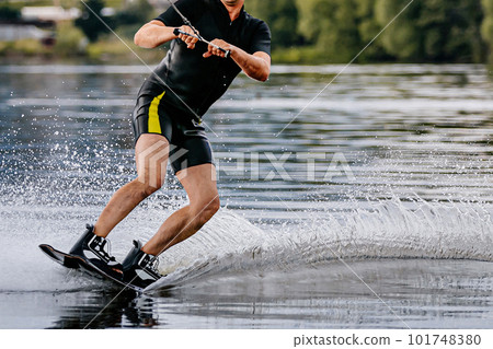 male athlete wakesurfing behind motorboat on pond, extreme summer water sports 101748380