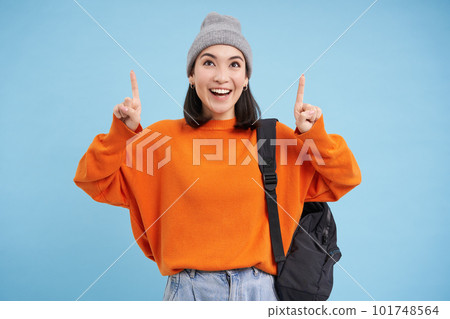 Happy korean girl points fingers up, shows advertisement, invites to click banner on top, stands over blue background Happy korean girl points fingers up, shows advertisement, invites to click banner on top, stands over blue background 101748564