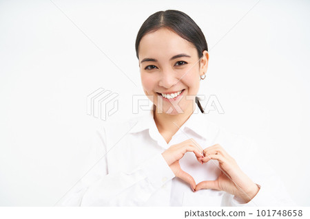 Portrait of lovely korean woman, office manager, shows heart hand sign and smiling, stands over white background Portrait of lovely korean woman, office manager, shows heart hand sign and smiling, stands over white background 101748658