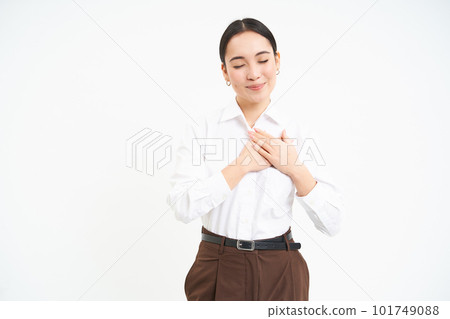 Romantic young asian woman holds hands on her heart with dreamy smile and eyes closed, white background 101749088