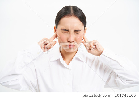 Annoyed young asian corporate worker, lady screams and shuts her ears with fingers, stands frustrated against white studio background 101749109